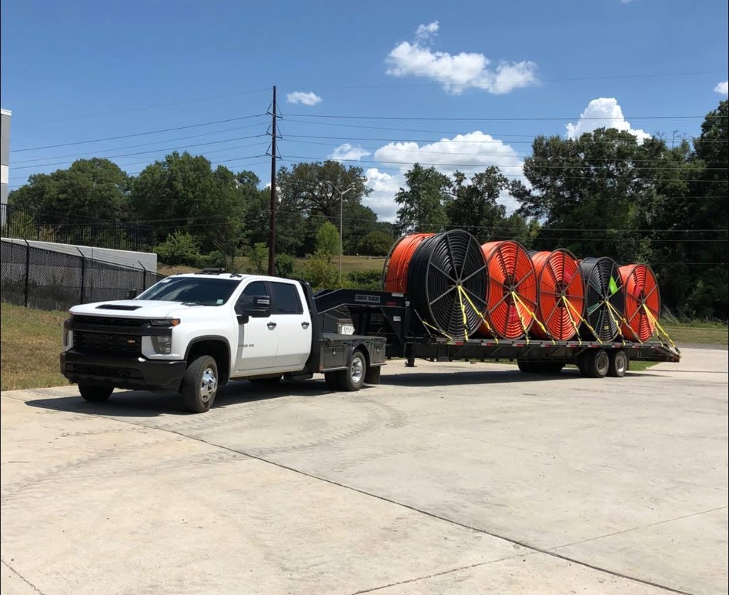Flatbed truck towing a trailer loaded with multiple conduit spools